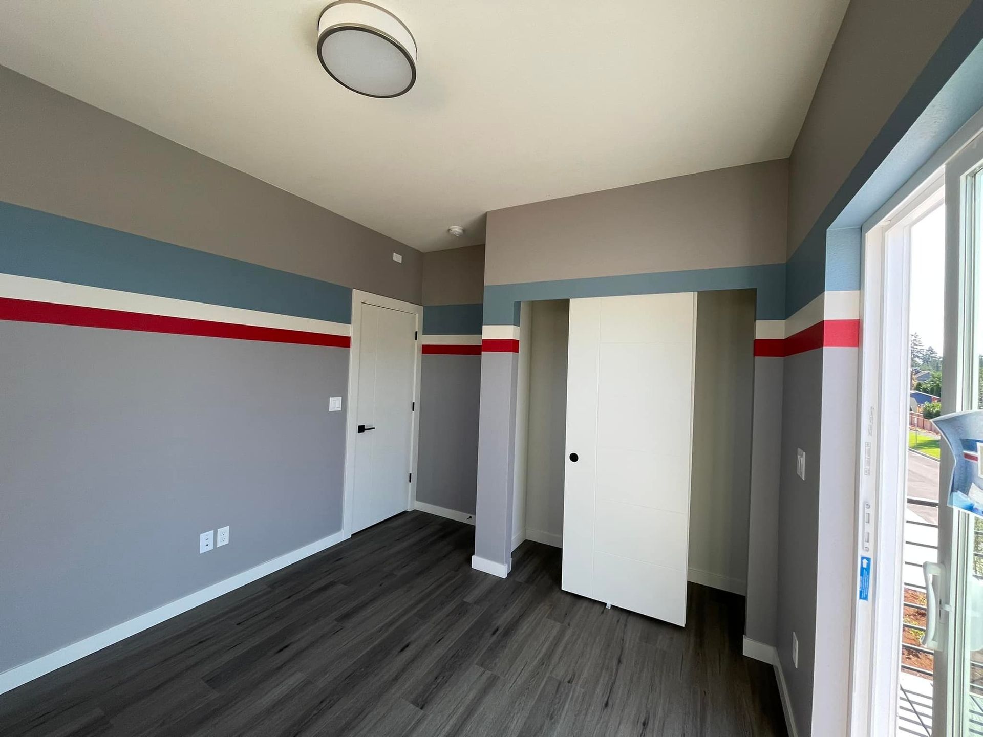 Empty room with dark wood flooring, light grey walls, and a decorative stripe of blue and red paint running horizontally.