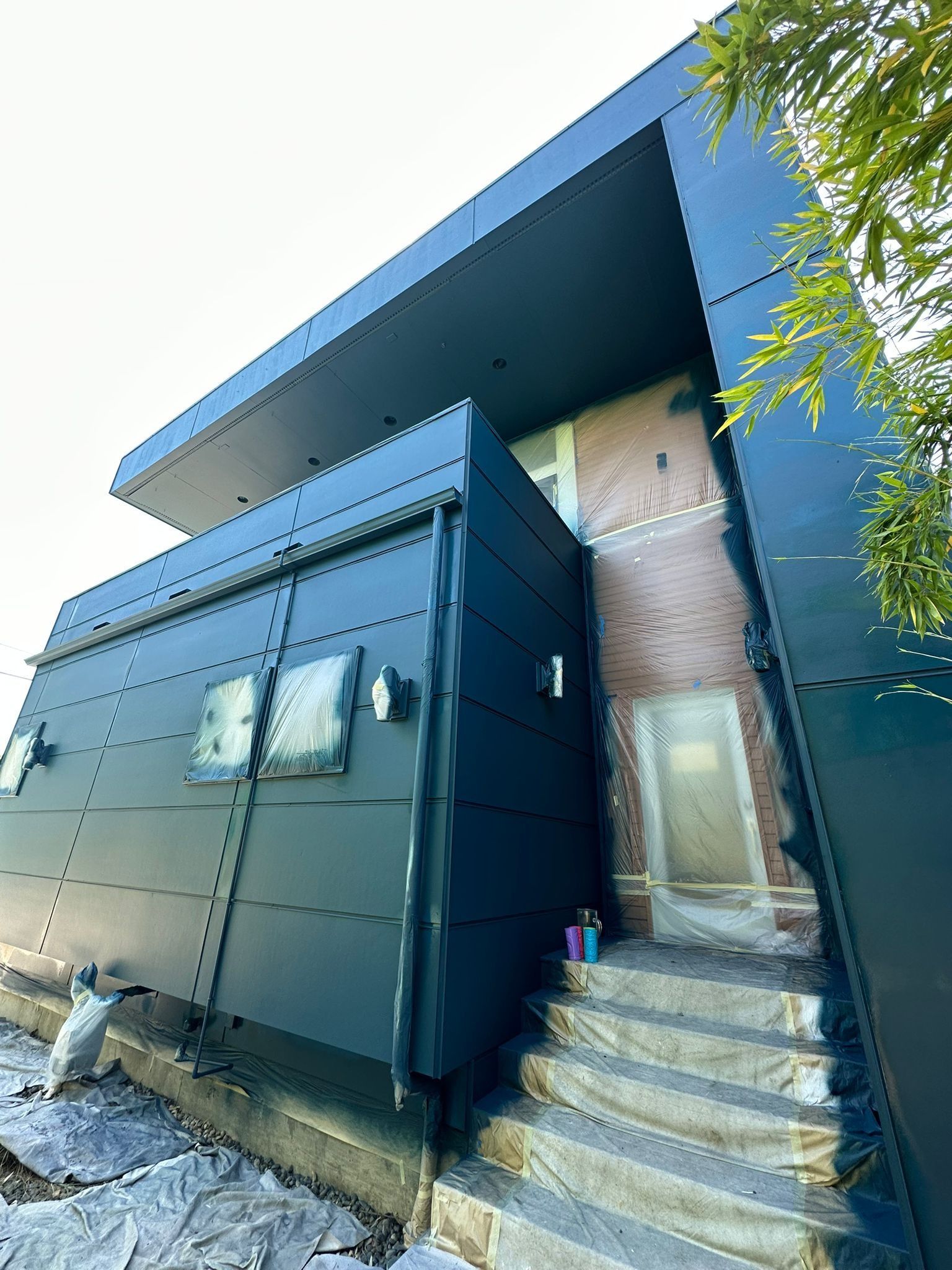 A low-angle view of a building exterior featuring contrasting dark blue modern paneling alongside a brick wall and steps.