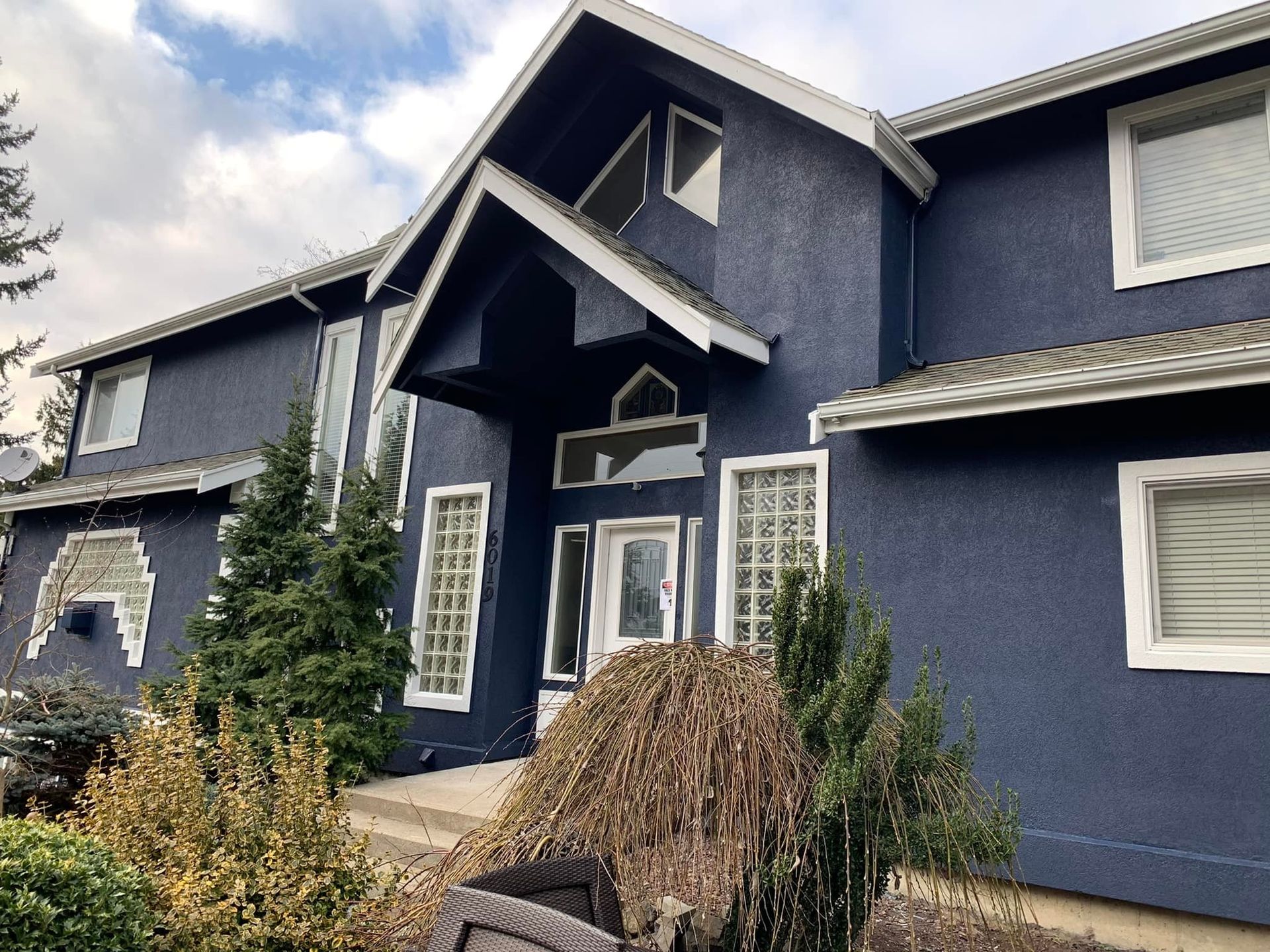 A large, two-story house with dark blue textured siding, white trim, and a prominent peaked entryway.
