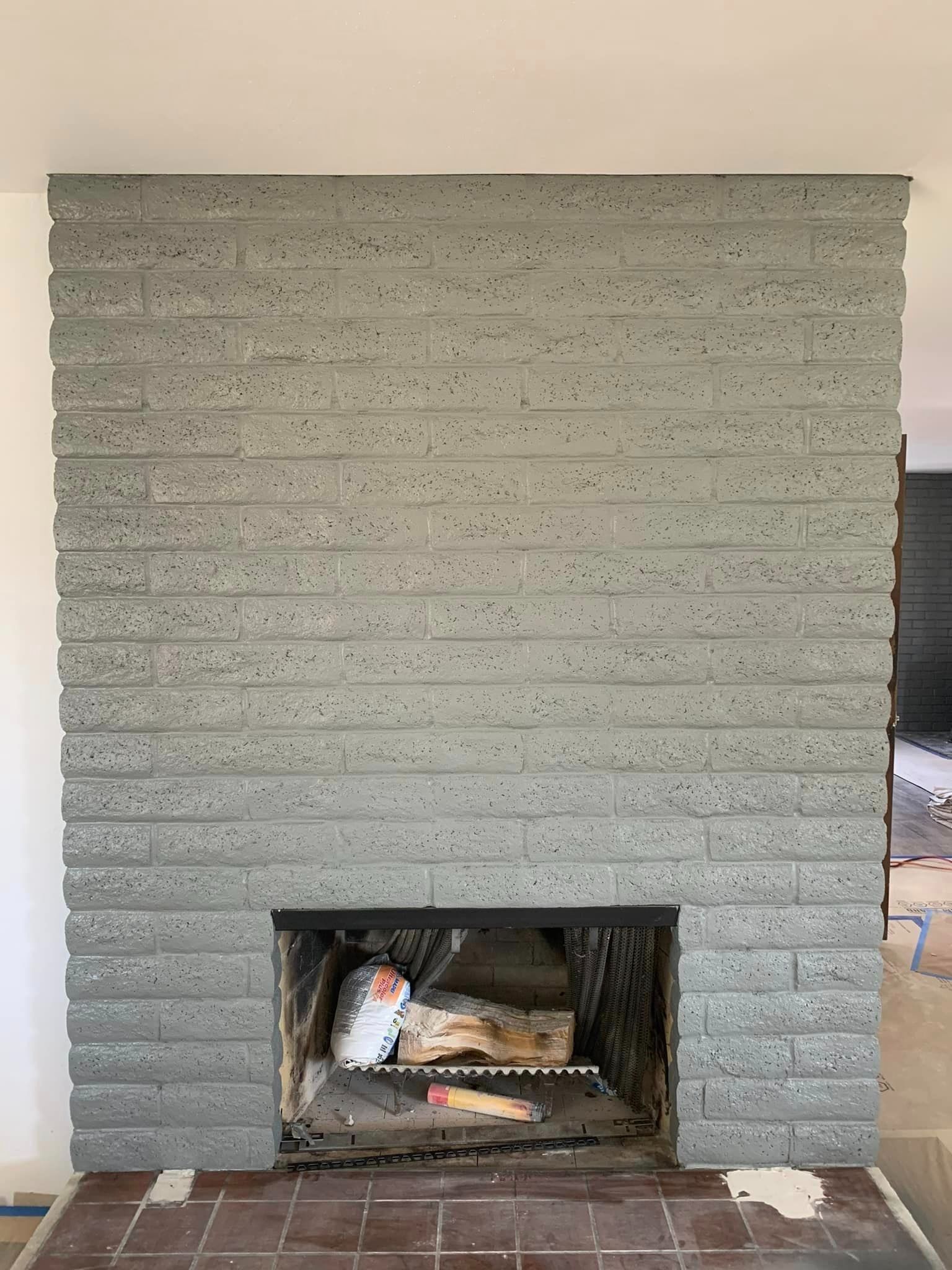 A gray painted brick fireplace with a firebox containing logs, set above a tiled hearth.