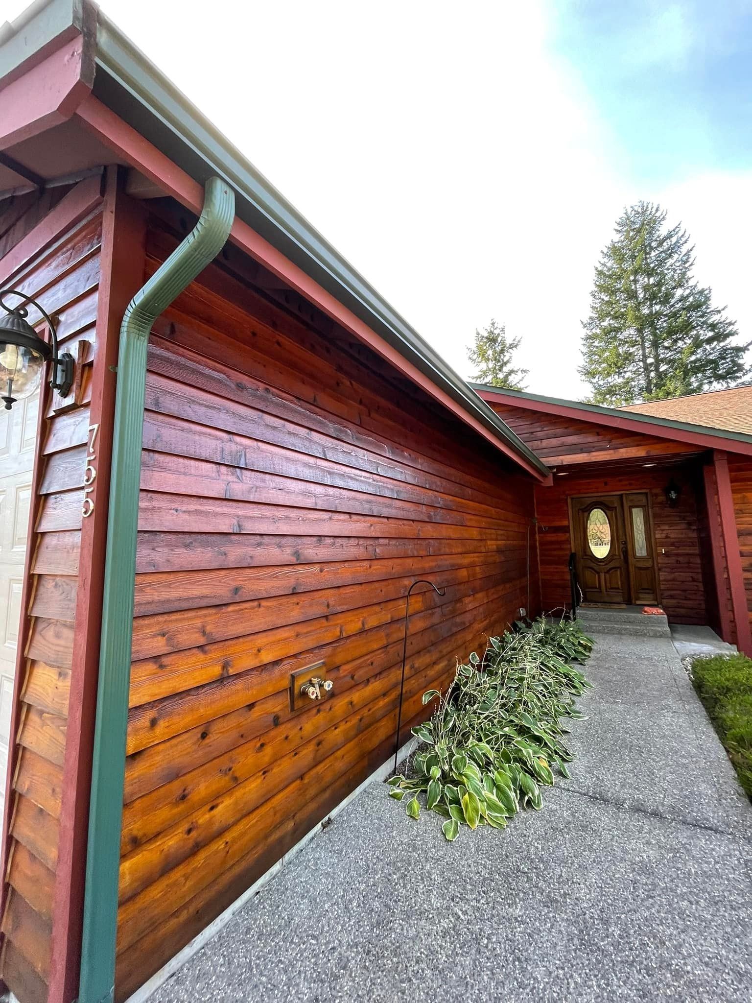 A side view of a home with stained wood horizontal siding, a green downspout, and a stone walkway leading to the entrance.