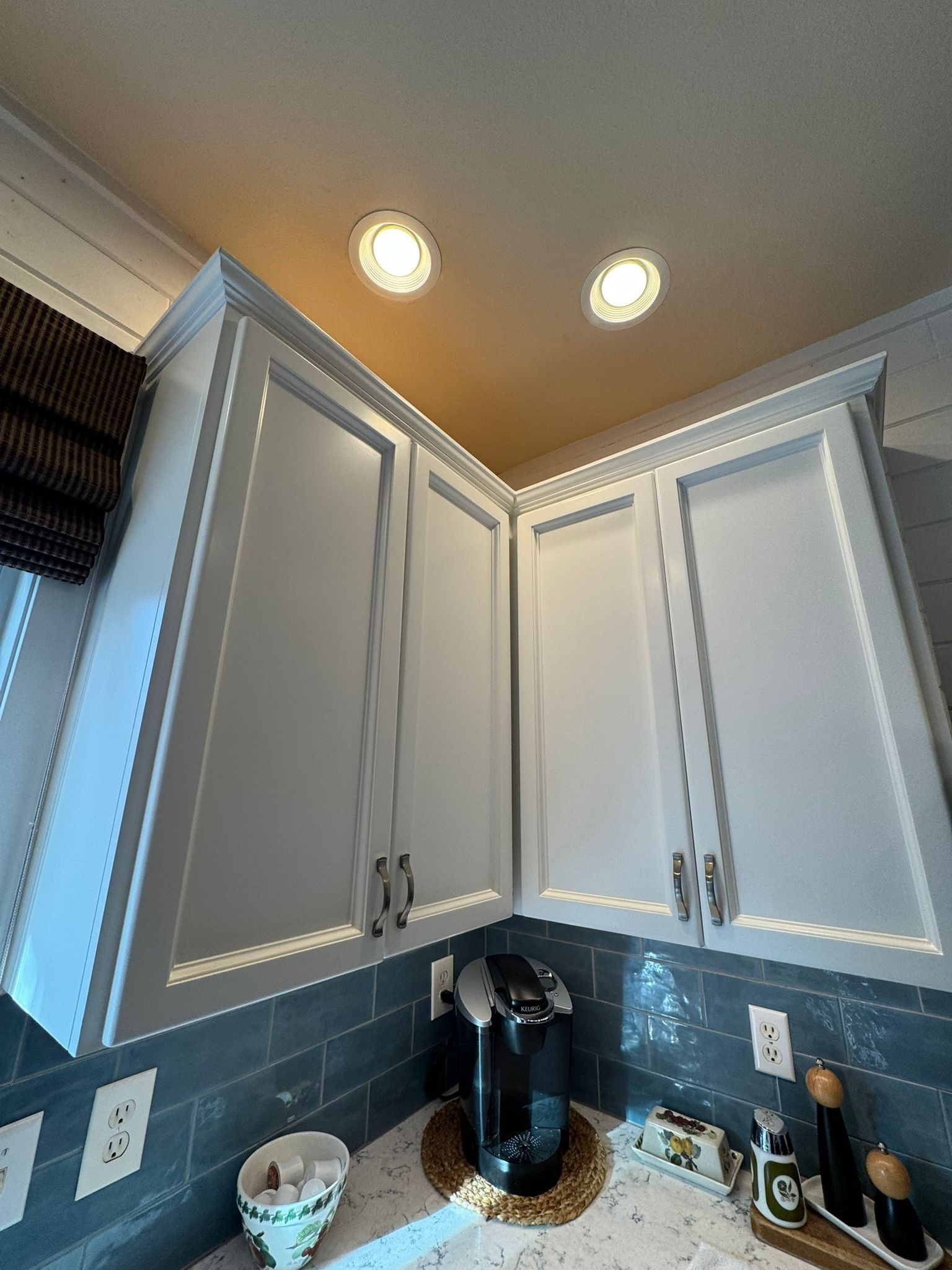 White corner kitchen cabinets with crown molding over a blue tiled backsplash and a coffee maker on the counter.