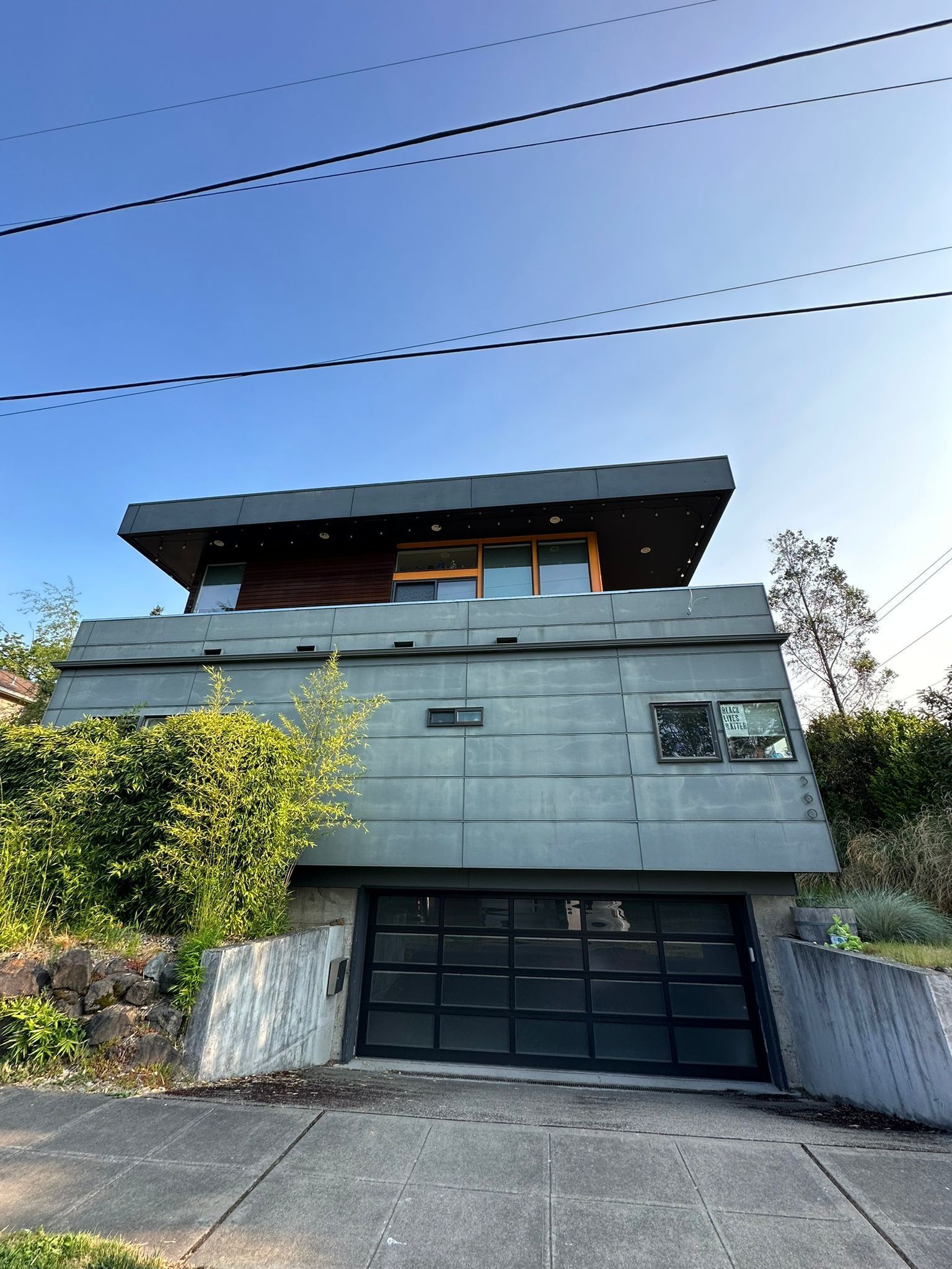 A modern, multi-level house with a dark, angular exterior, paneled siding, and a large black glass garage door.
