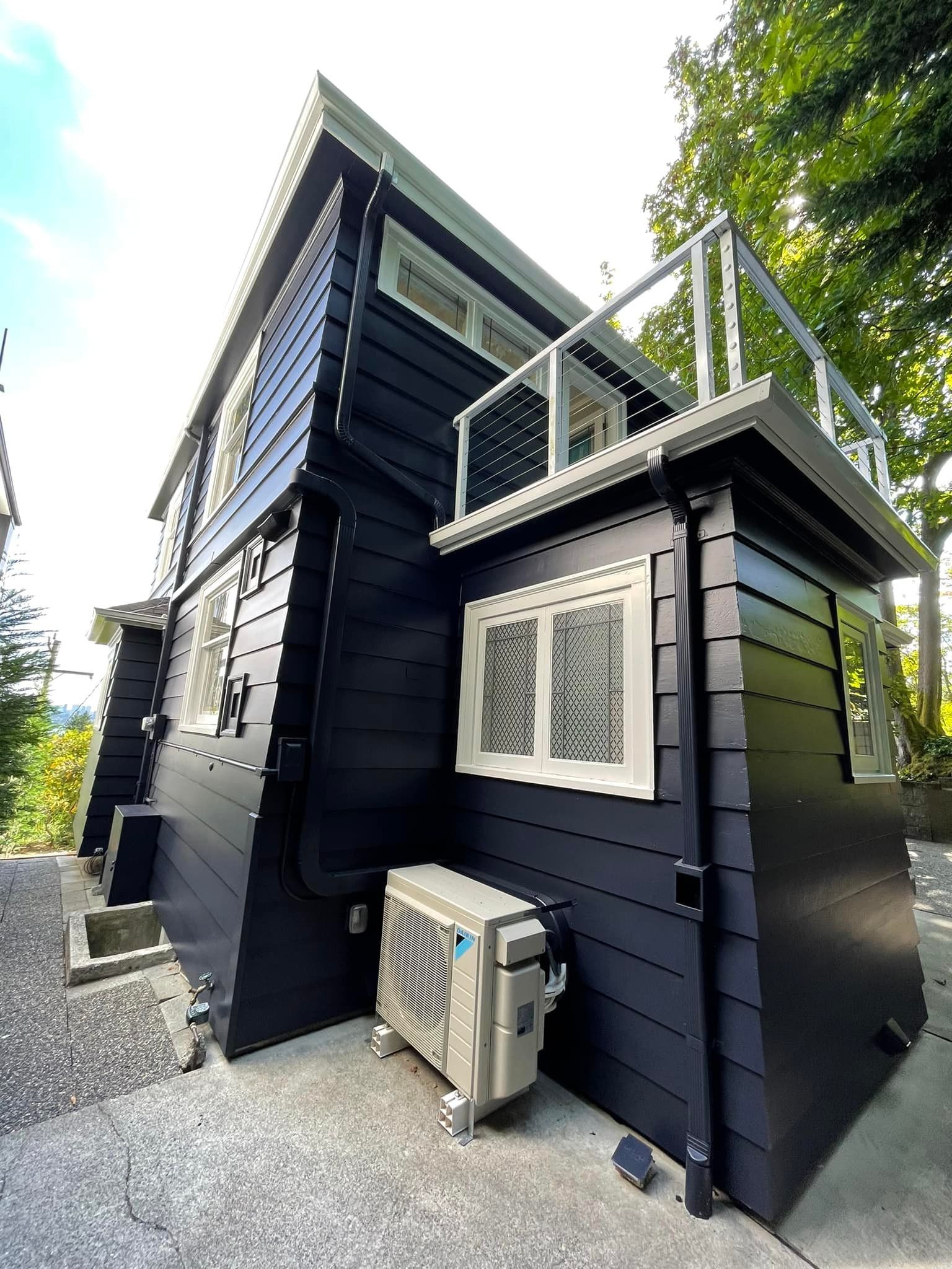 Low-angle view of a modern house exterior with dark horizontal siding, white trim, and a small balcony.
