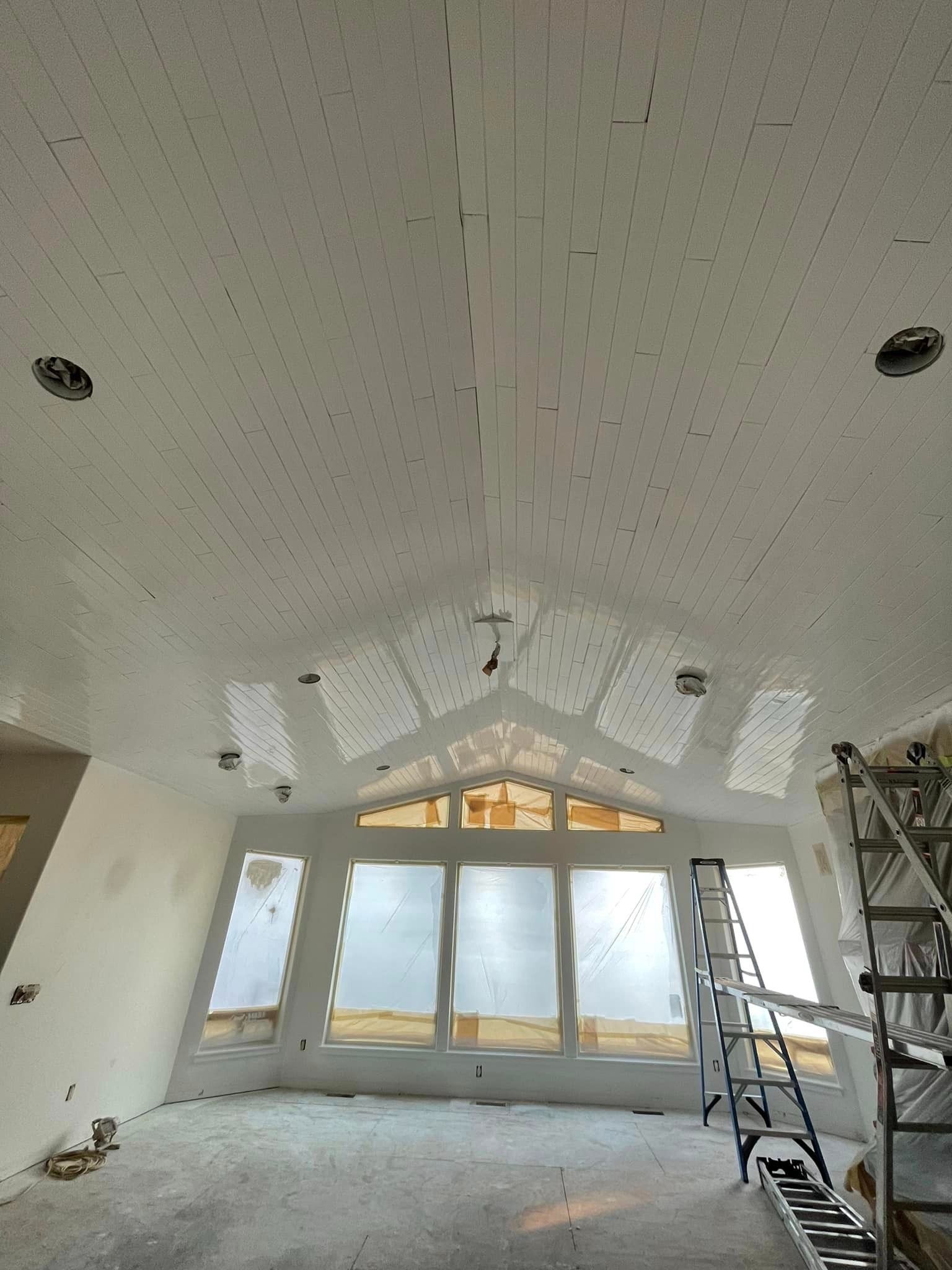 Interior view of a vaulted room under construction, featuring acoustic ceiling tiles, recessed lights, and large windows.