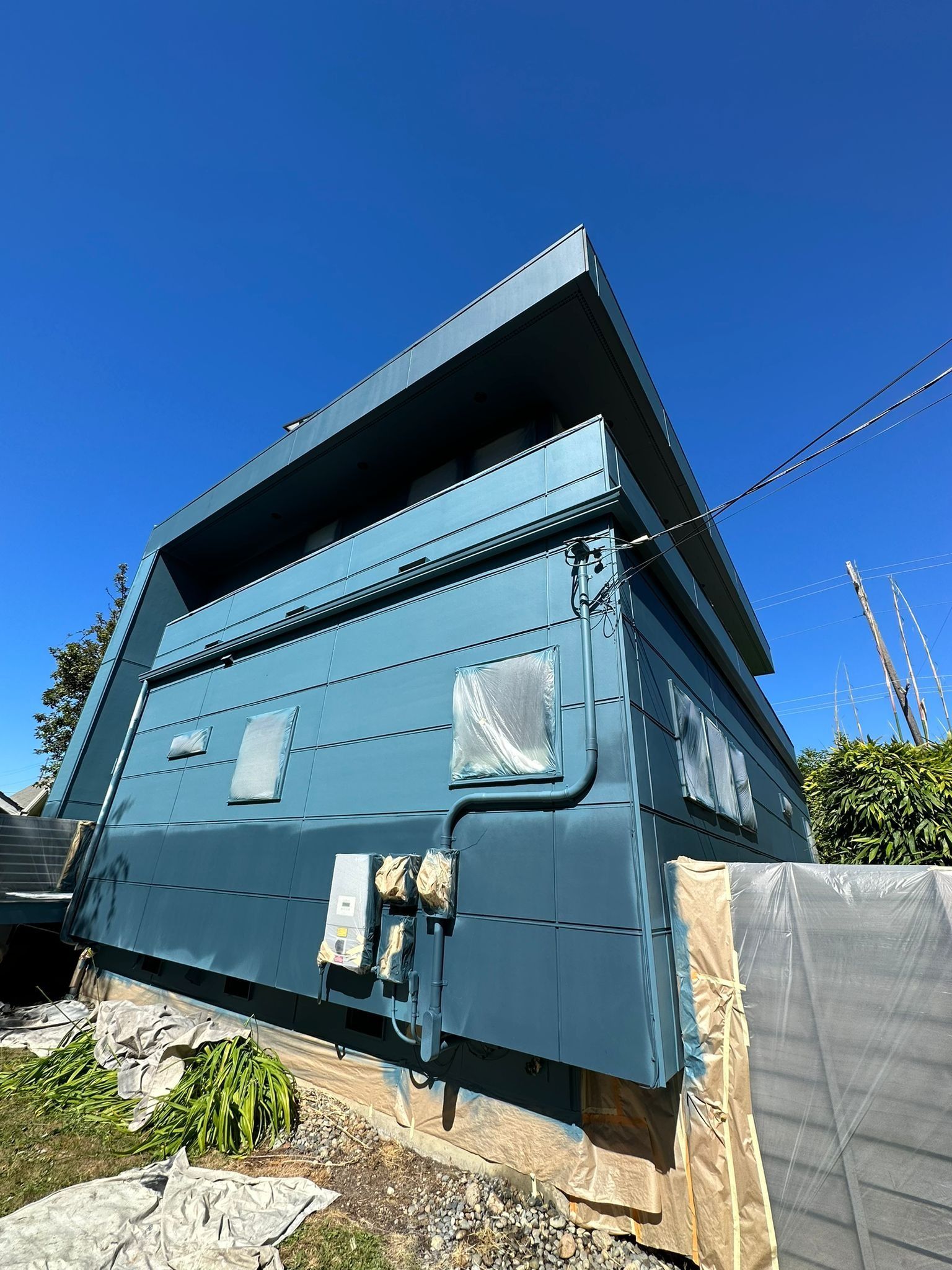 A blue, modern slanted-roof building exterior on a bright sunny day, with exposed building materials visible at the base.