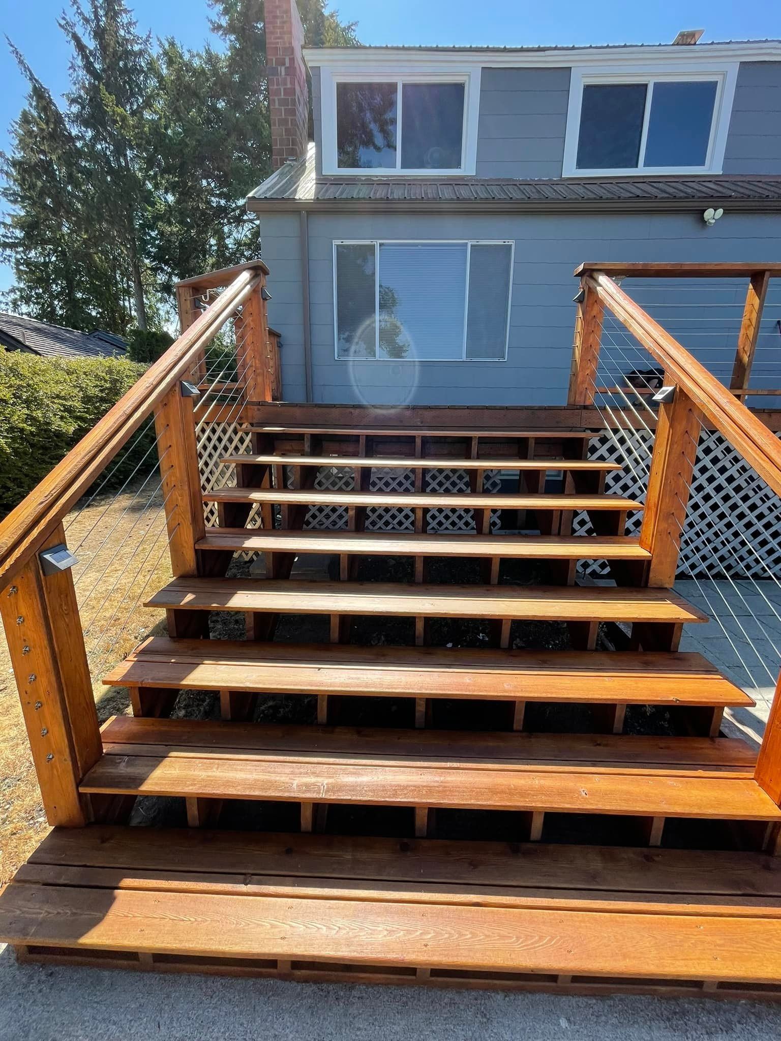 Wooden steps with railings leading up to the back of a grey house with white trim.