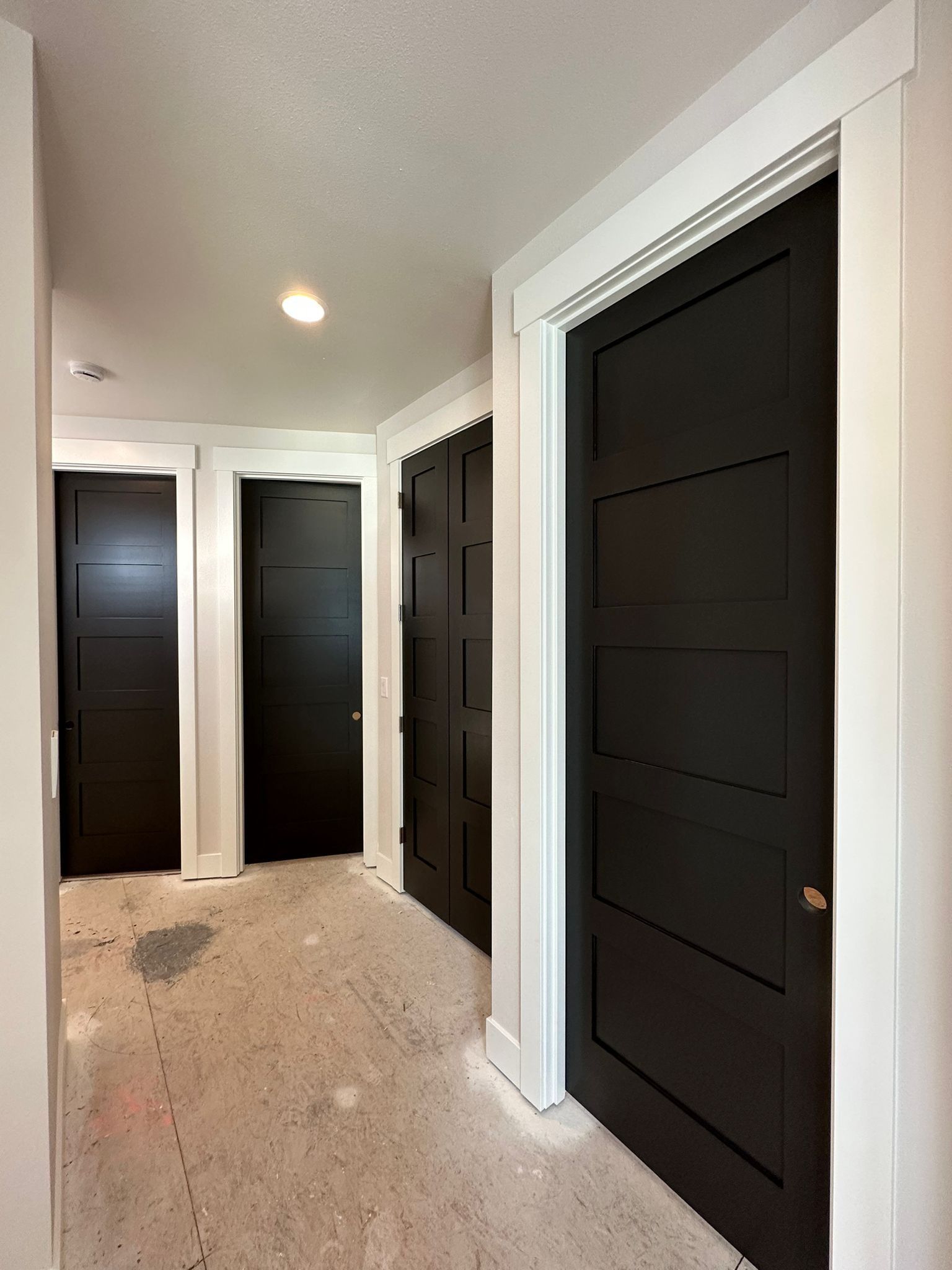 A hallway with white trim and multiple black, five-panel doors under construction.