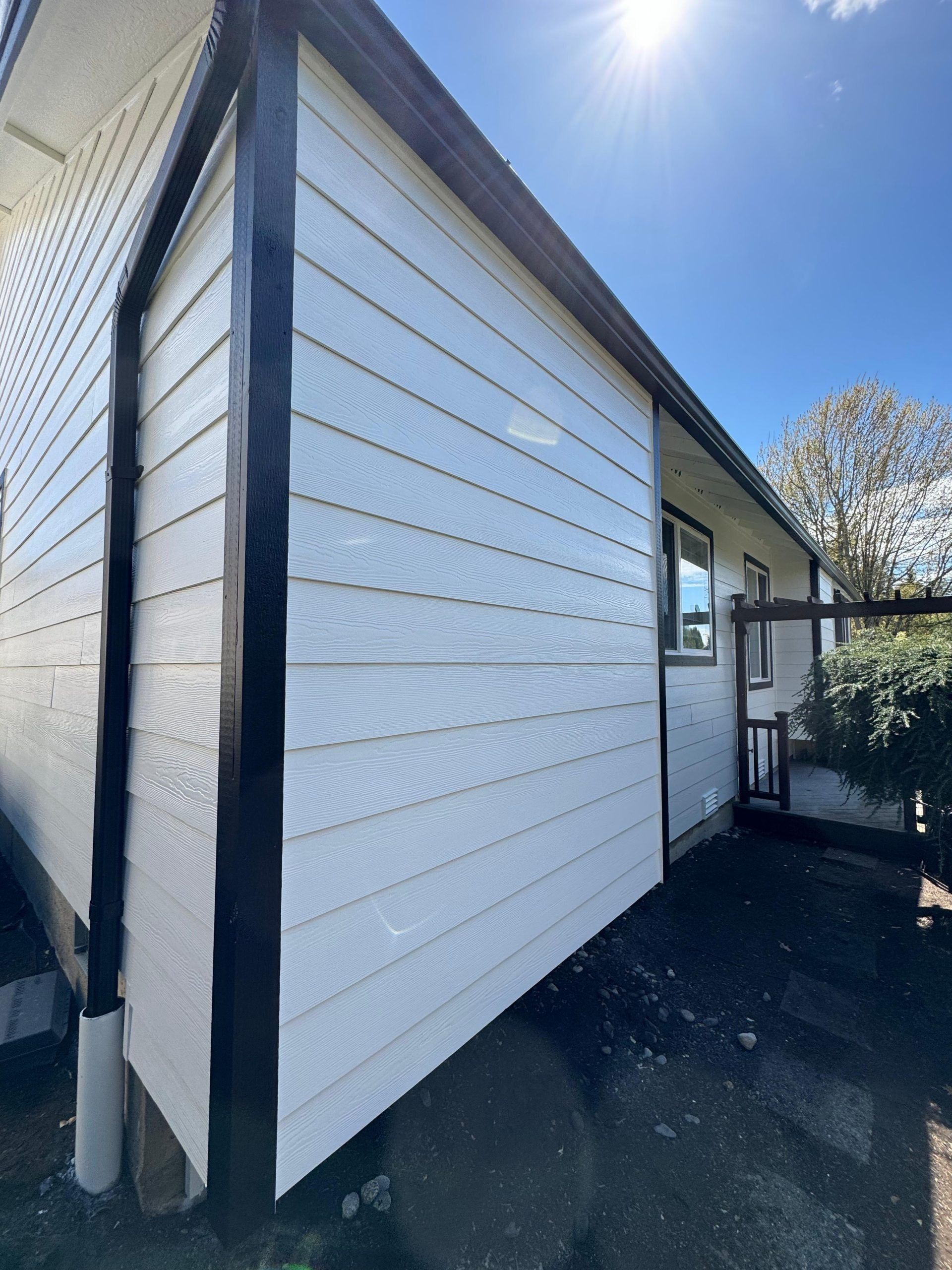 A side view of a house exterior with white horizontal siding and dark trim under a clear blue sky.