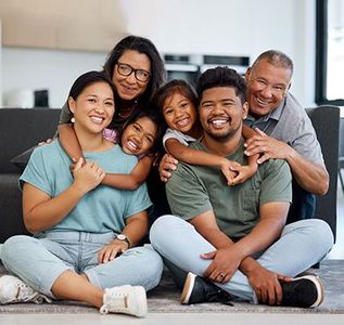 A smiling, multi-generational family sitting together on the floor of a bright, modern living room.