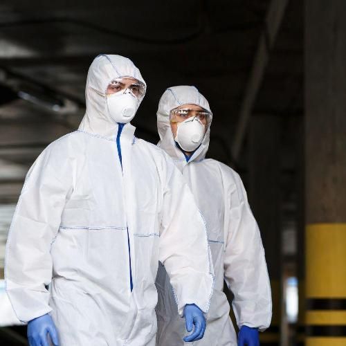 Two people in white hazmat suits, masks, and goggles walking indoors.