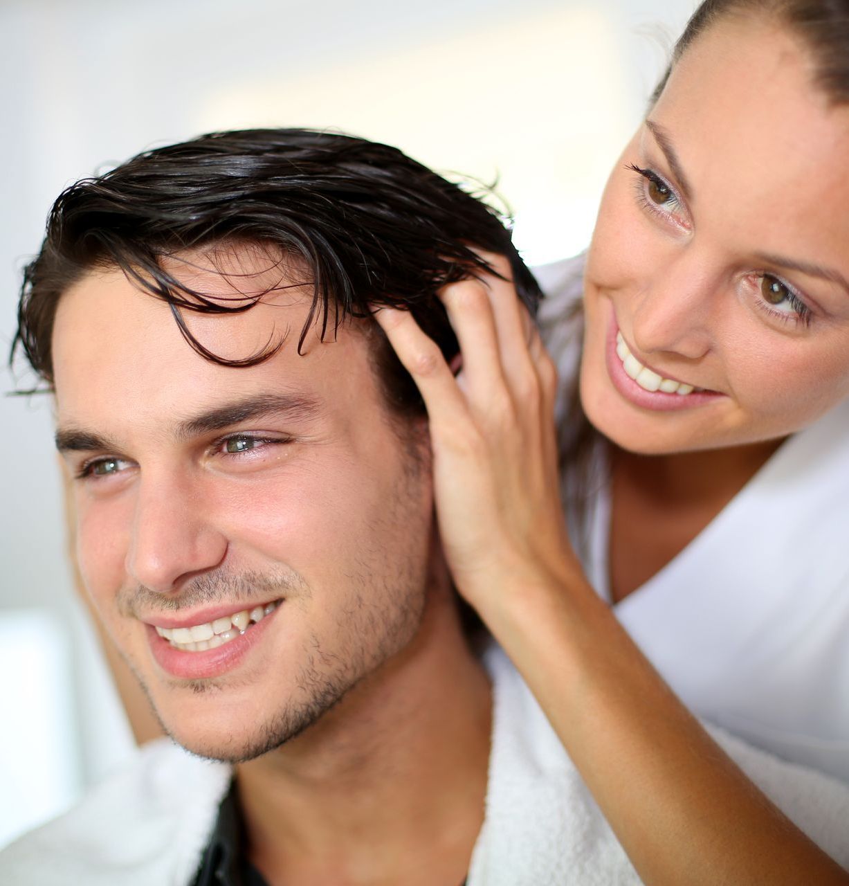 A woman is touching a man 's hair and smiling