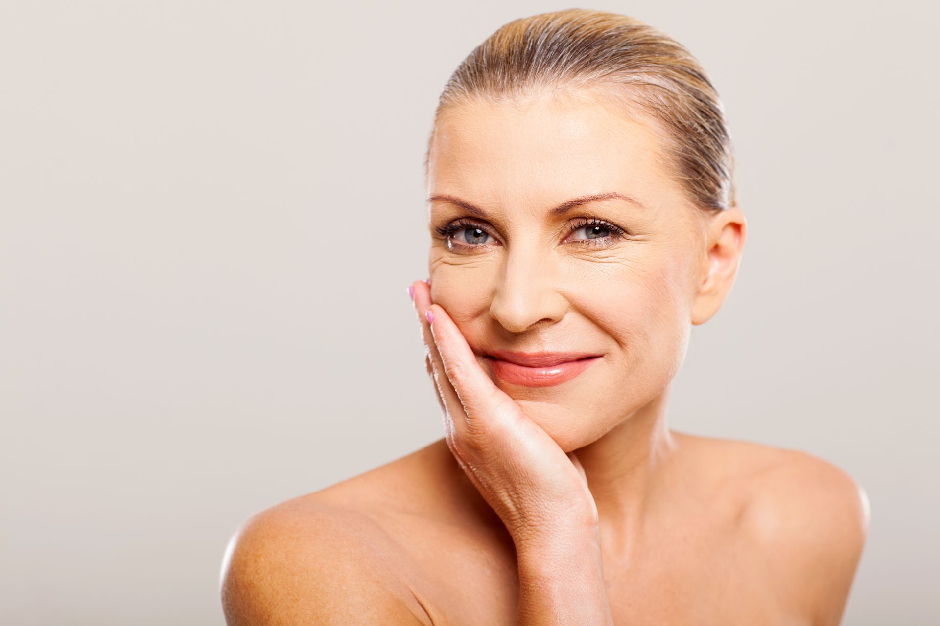 A woman is touching her face with her hand and smiling.
