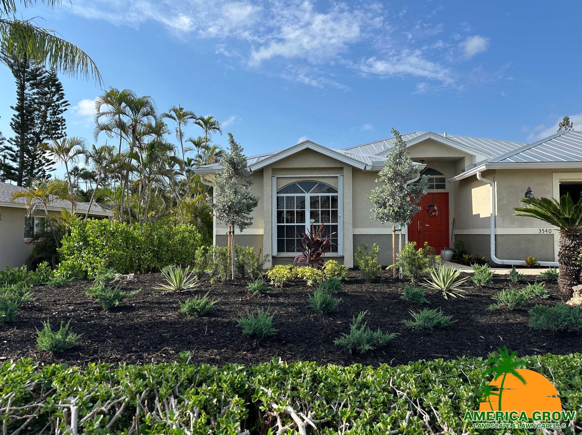 House exterior with lush landscaping, featuring dark mulch and green plants under a blue sky.