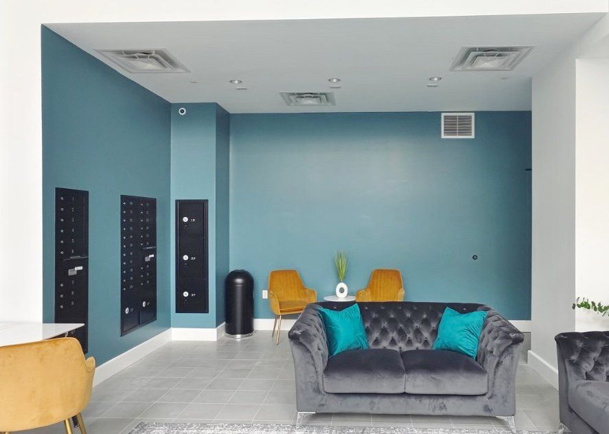 Modern lobby with teal walls, a gray sofa, yellow chairs, and mailboxes.