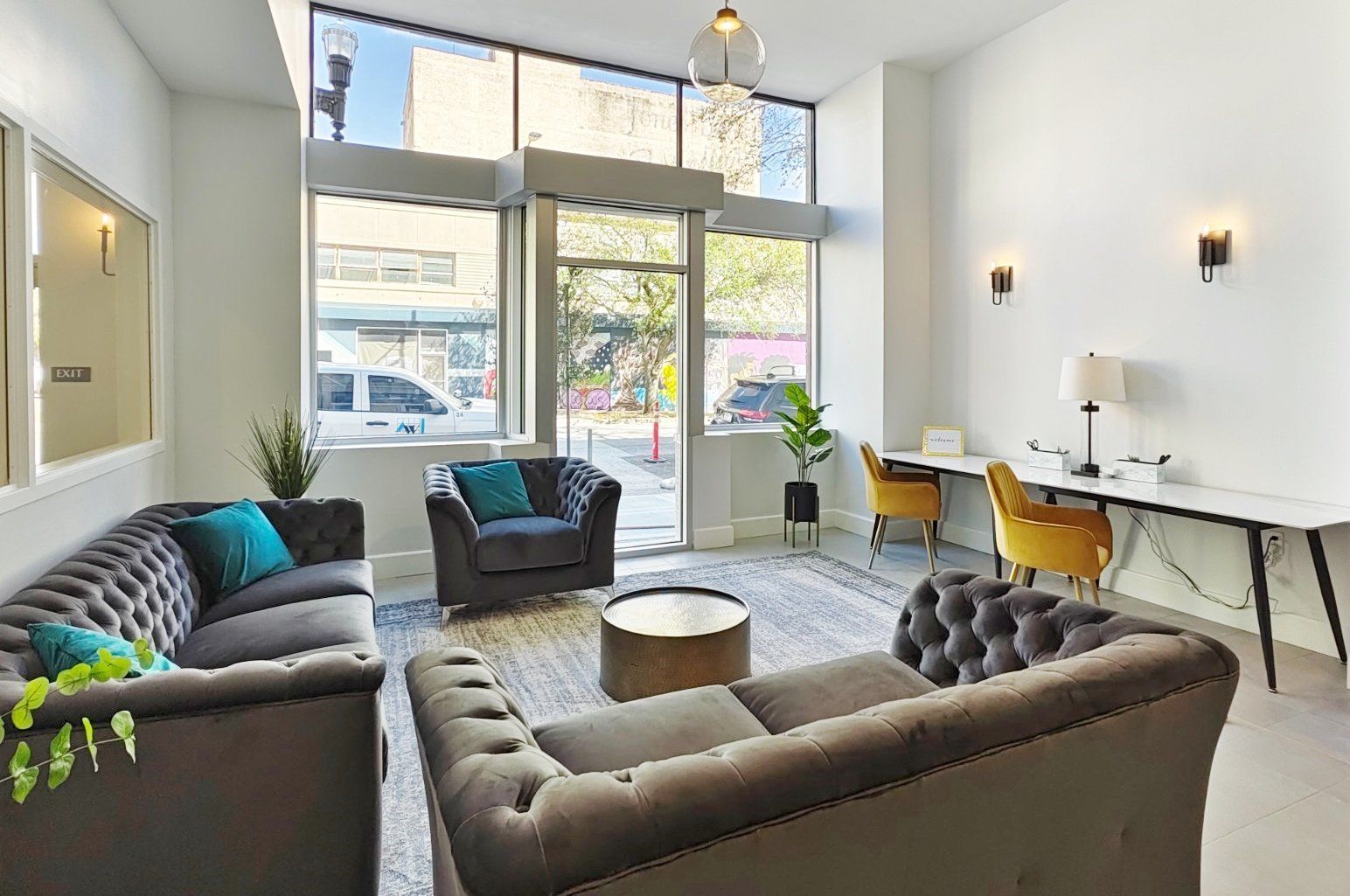 A modern lobby with tufted couches, chairs, desk, and large windows looking out onto a street.