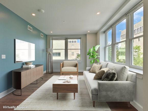 Living room with light blue walls, a gray couch, and large windows with city views.
