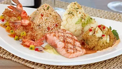 Plate of grilled salmon, shrimp, rice, and cauliflower, on a white plate.