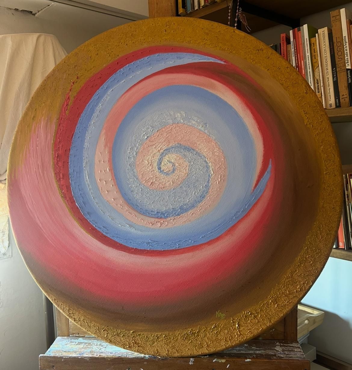 Cuadro circular con diseño en espiral de color rosa, azul y dorado.