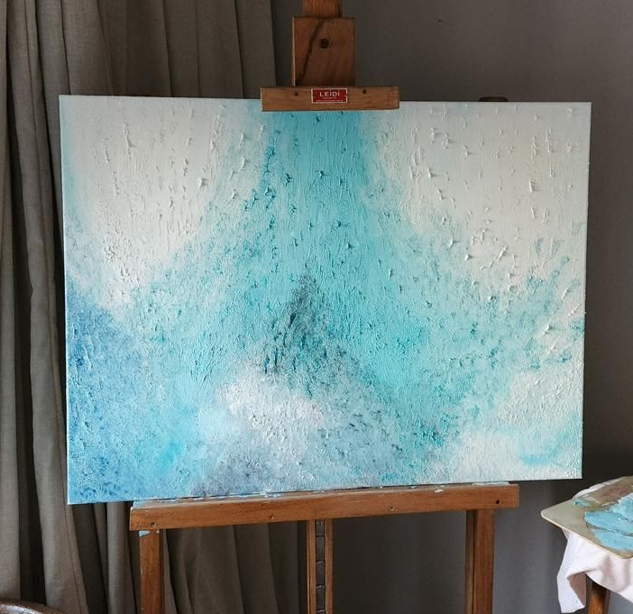 Pintura abstracta con textura azul y blanca sobre un caballete.