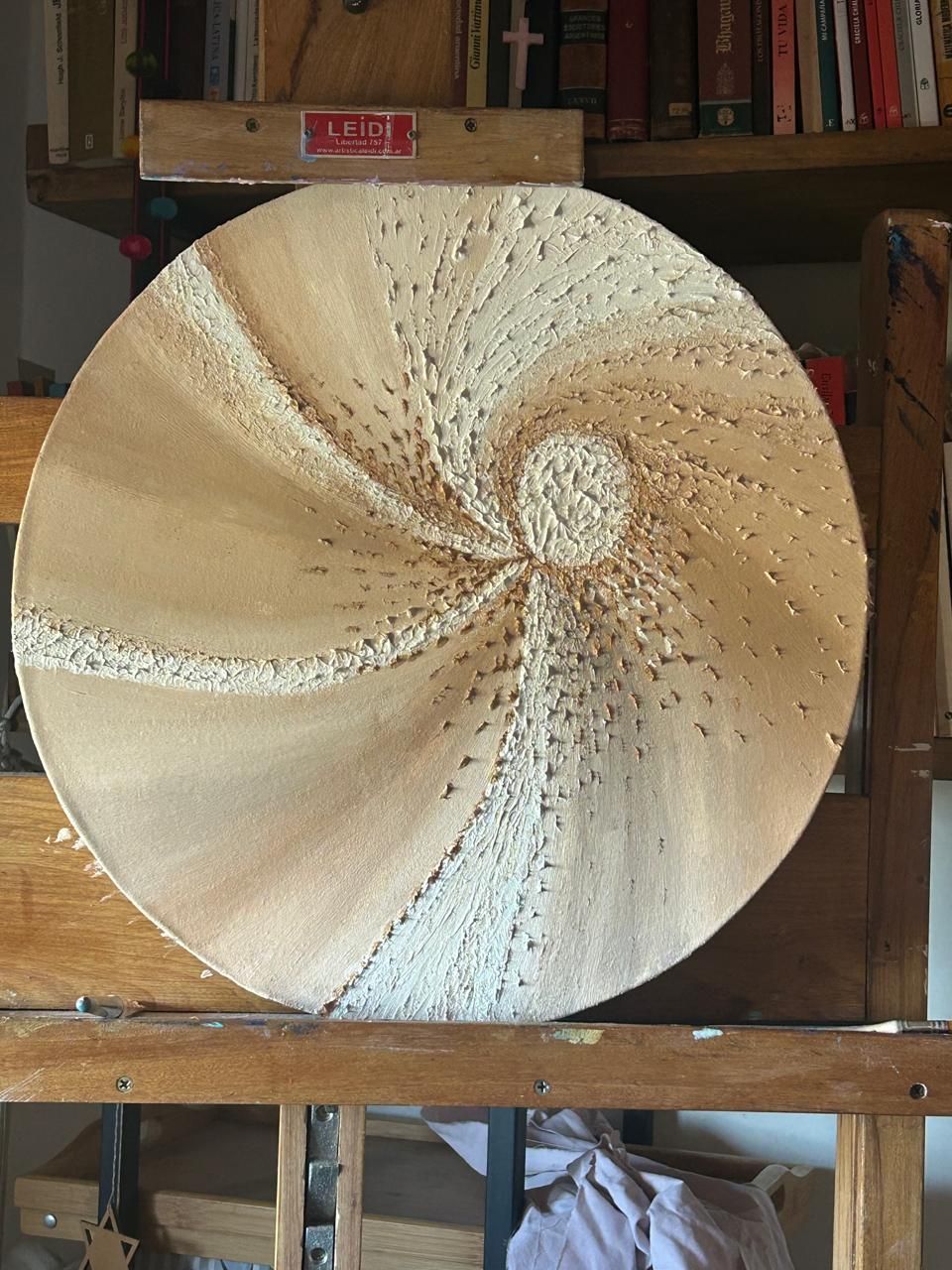 Pieza de arte en madera con patrón de remolinos, tonos marrón claro y beige.