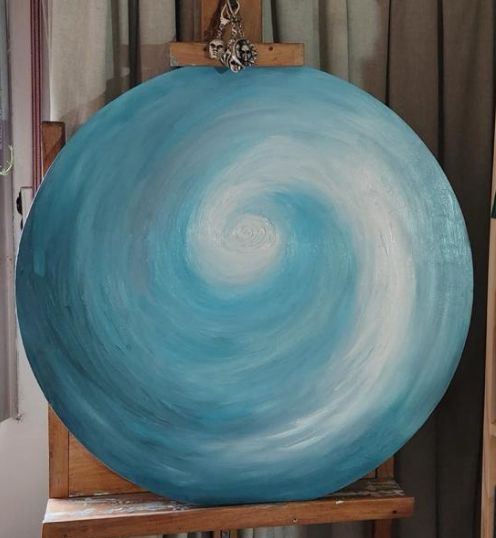 Pintura en espiral azul y blanca sobre lienzo redondo, expuesta en un caballete.