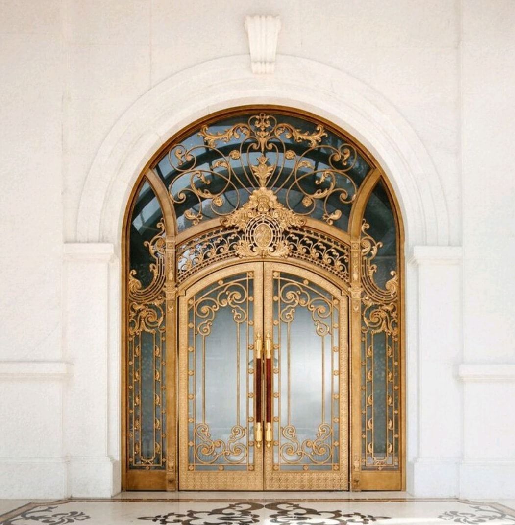 Ornate gold double doors with an arched glass transom in a white stone doorway