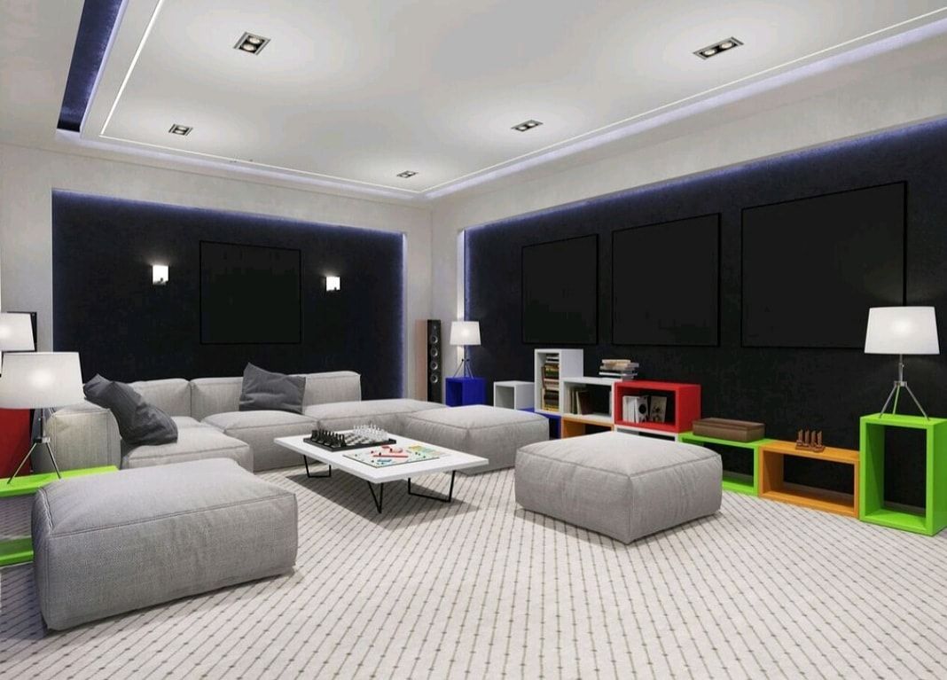 Modern living room with black windows, gray sofas, white rug, and colorful shelves along the wall