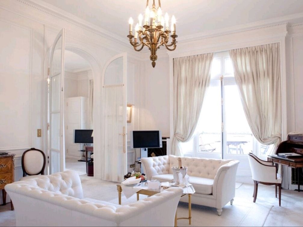 Elegant white living room with tufted sofas, chandelier, and tall windows with curtains