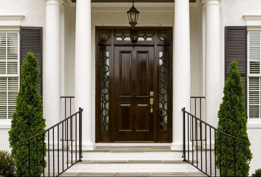 Front entrance with dark wood door, white columns, black railings, and potted shrubs