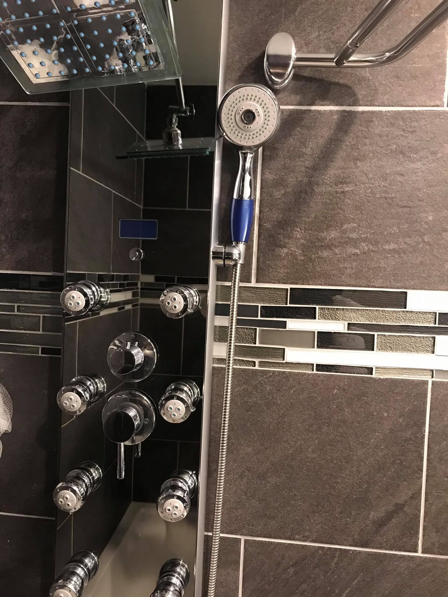 Modern black-and-chrome shower with rainfall head, handheld sprayer, and body jets on tiled walls