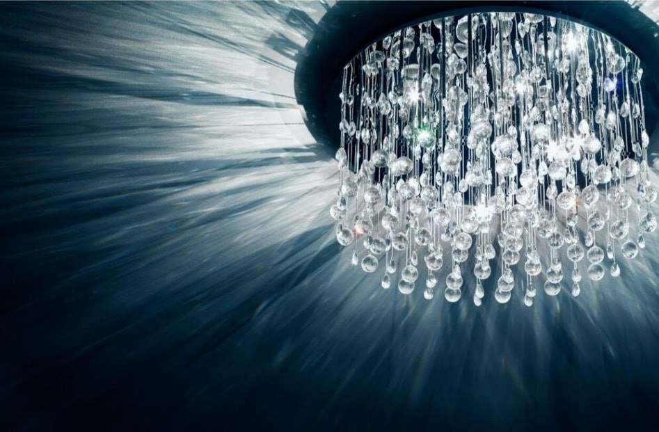 Crystal chandelier casting blue light and reflections on a dark ceiling