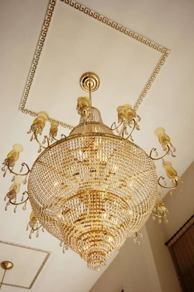 Large ornate gold chandelier hanging from a high white ceiling in an elegant room