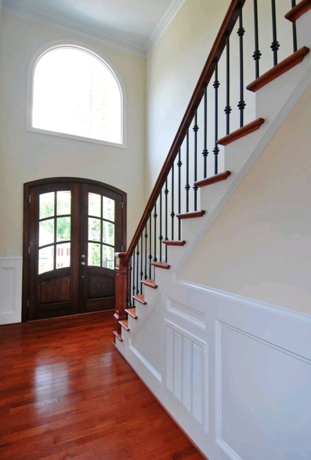 Bright foyer with hardwood stairs, dark wood handrail, arched window, and double front door