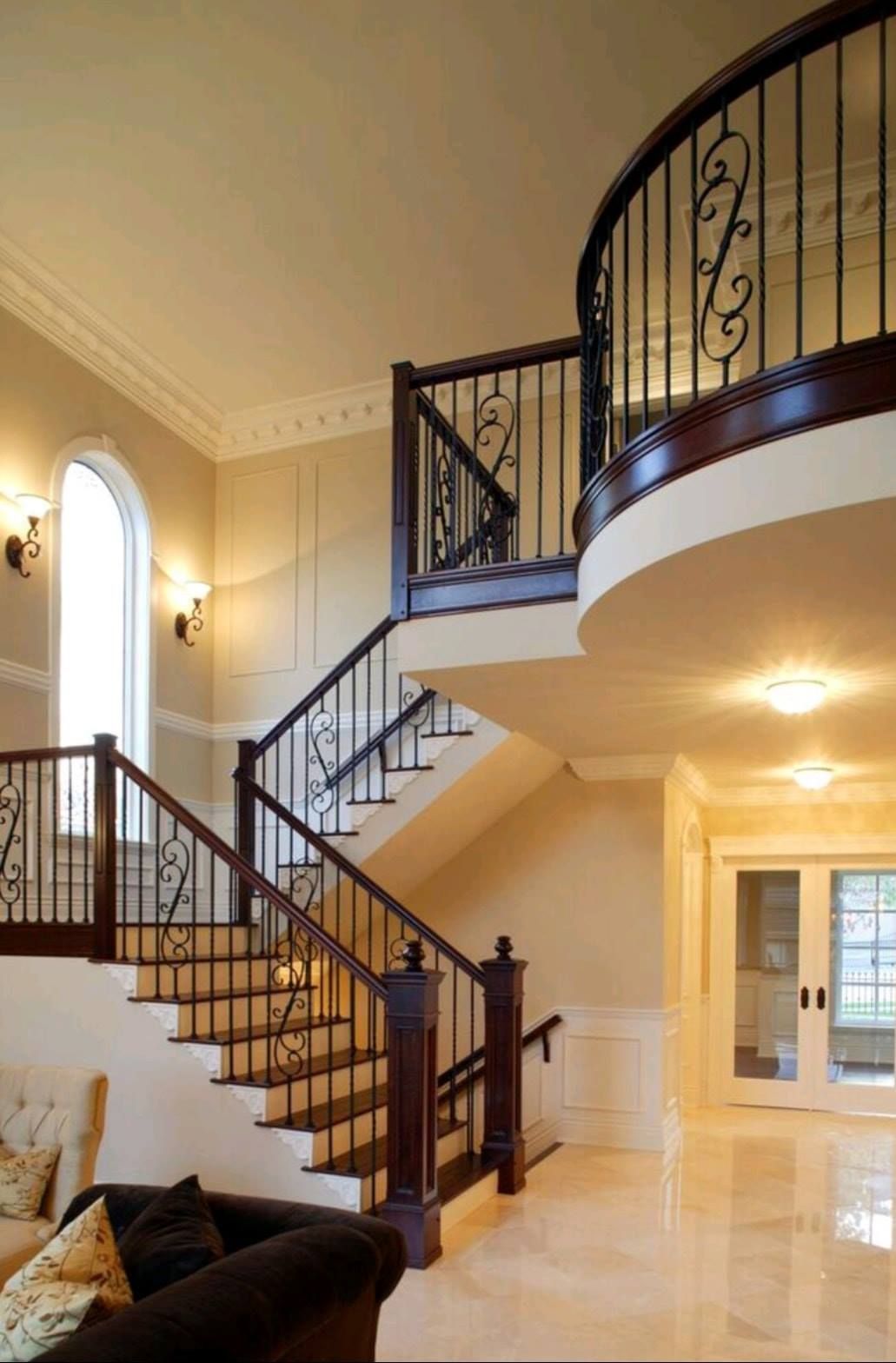 Elegant foyer with curved staircase, wrought-iron railing, marble floor, and arched windows