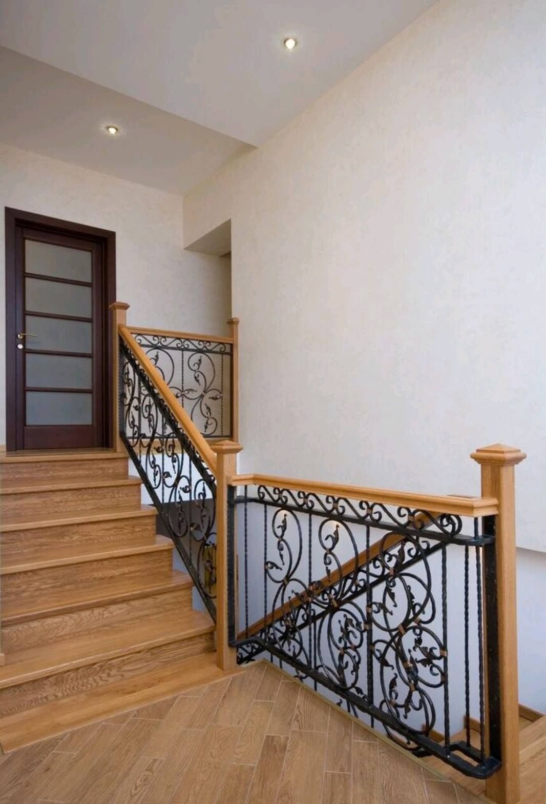 Indoor staircase with wood steps, ornate black iron railing, and beige walls.
