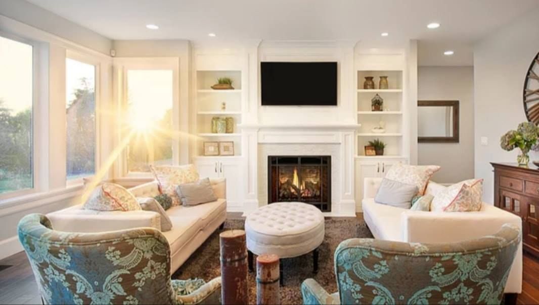 Bright living room with white fireplace, beige sofas, teal chairs, and sunlight streaming through windows