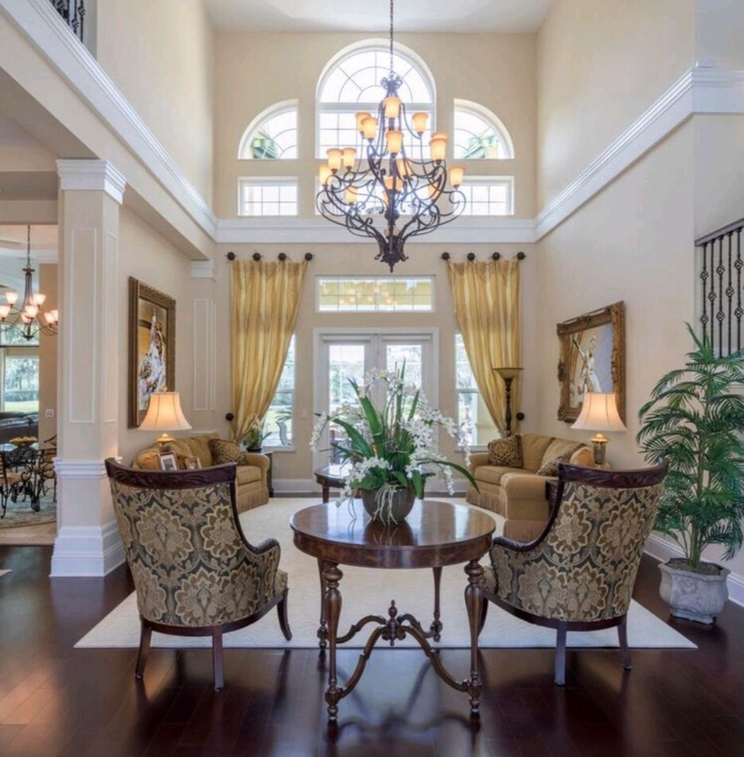 Elegant foyer with a chandelier, high ceiling, arched window, and ornate chairs around a round table