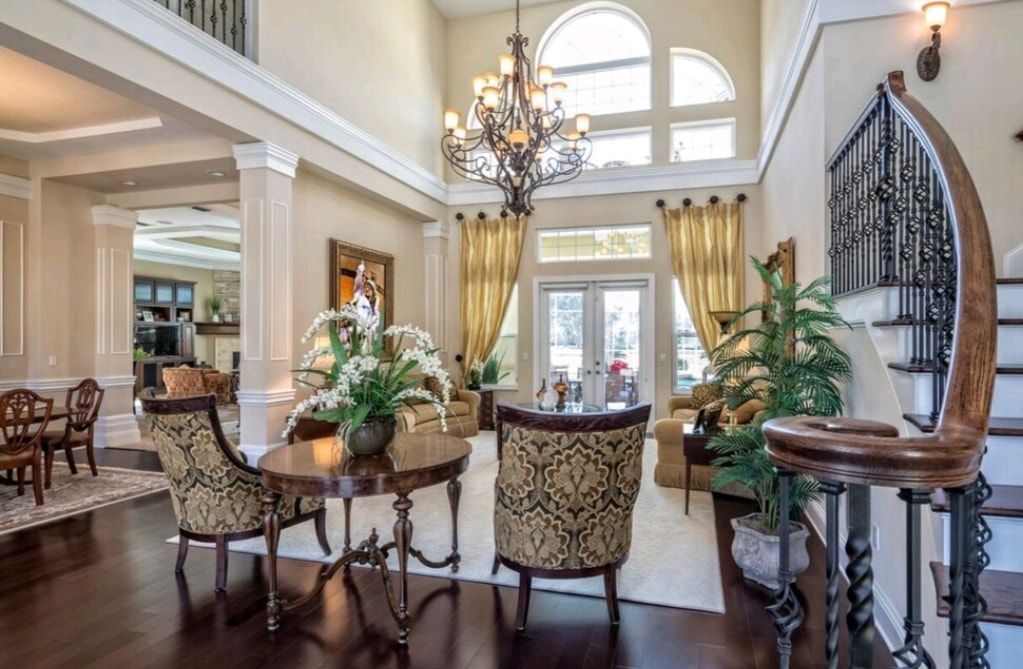 Elegant foyer with a chandelier, arched windows, staircase, and ornate chairs around a round table