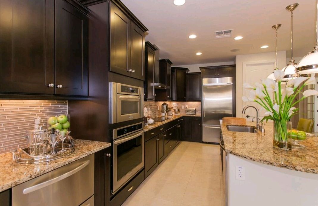 Modern kitchen with dark cabinets, granite counters, stainless appliances, and island lighting