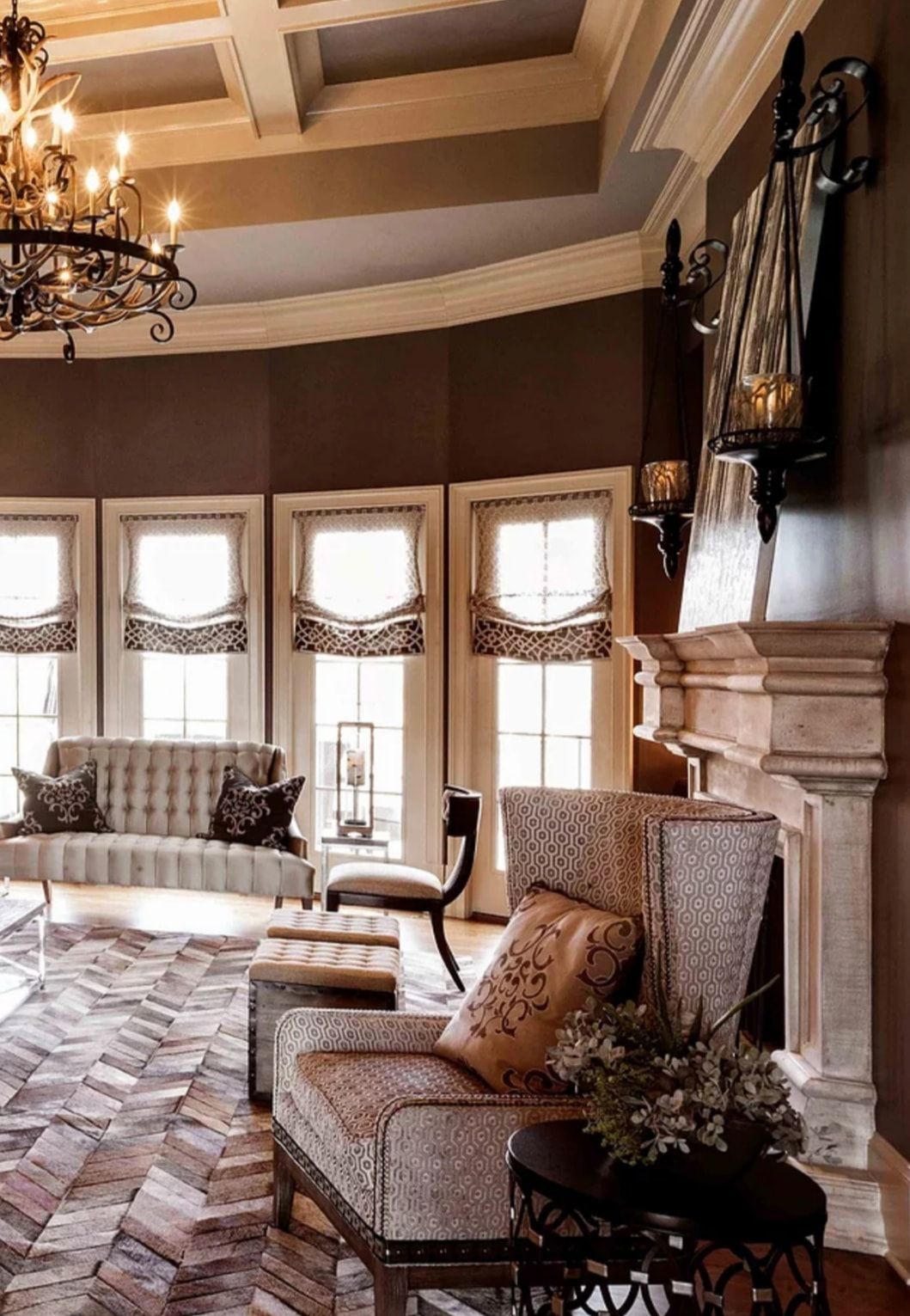 Elegant living room with large windows, patterned chairs, chandelier, and stone fireplace