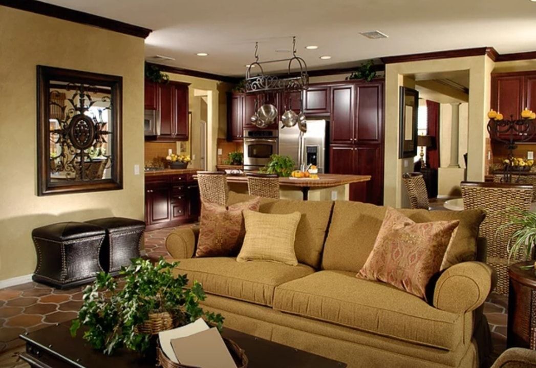 Warm living room with beige sofa, dark wood cabinets, and a kitchen opening in the background