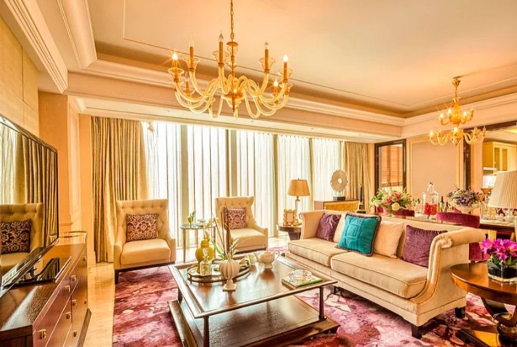 Luxurious living room with cream sofas, gold decor, chandelier, and sunlight through tall curtains
