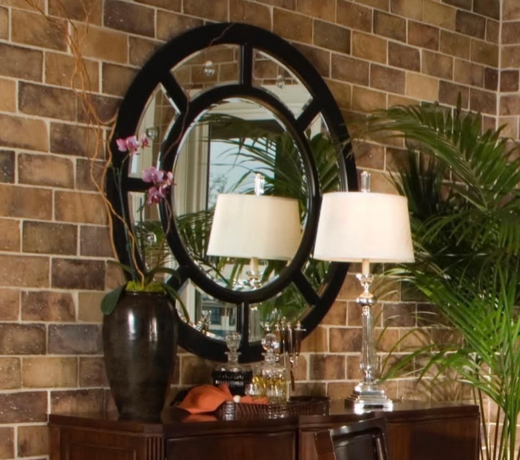 Decorative mirror and lamps on a wooden console against a brick wall, with a vase and palm leaves