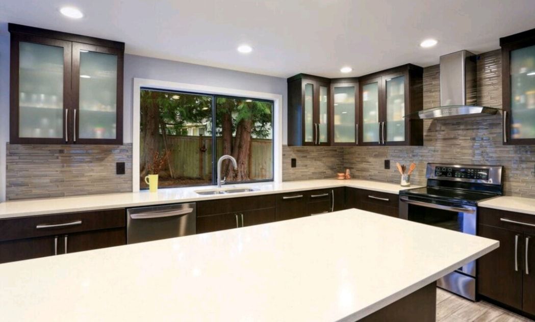 Modern kitchen with white island, dark cabinets, stainless appliances, and a large window over the sink