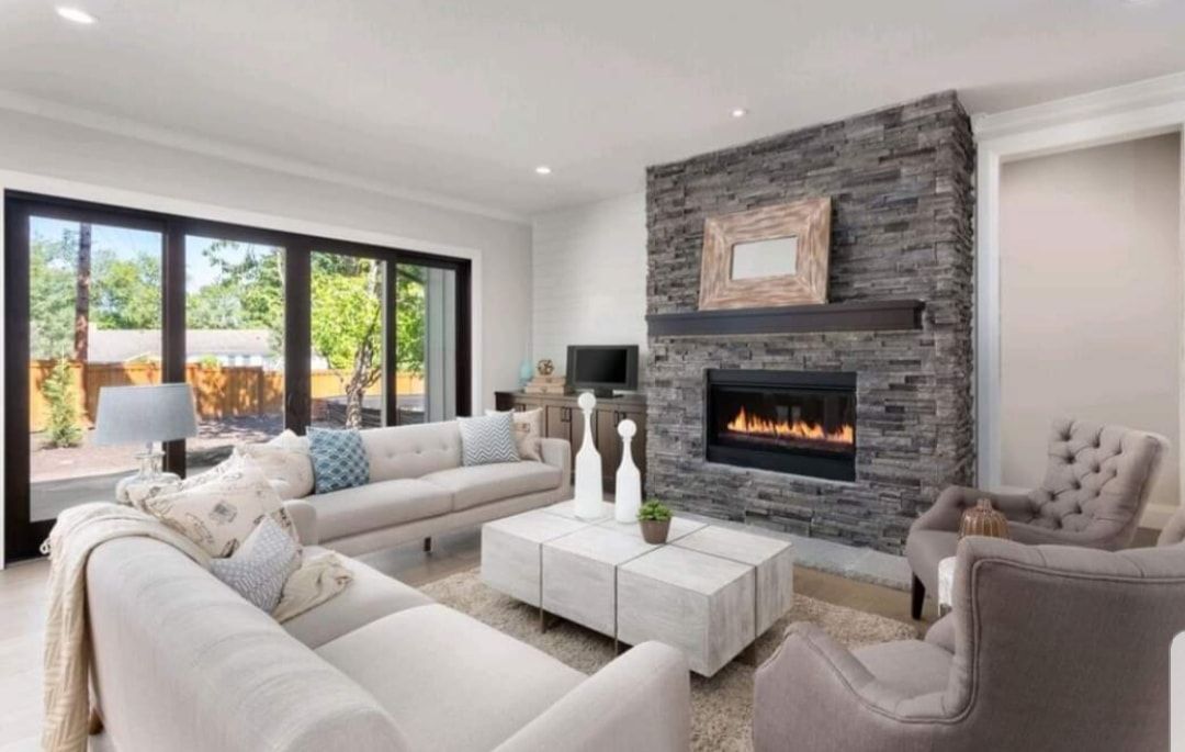 Bright modern living room with white sofas, stone fireplace, and large glass doors overlooking a patio