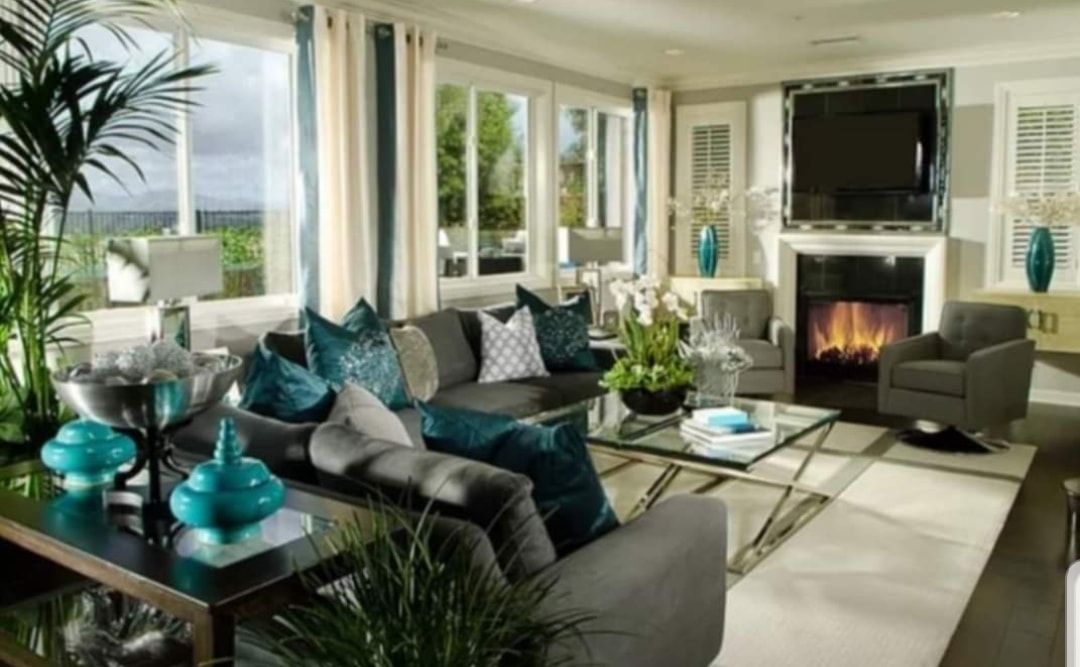 Bright modern living room with gray sofas, teal accents, fireplace, TV, and large windows