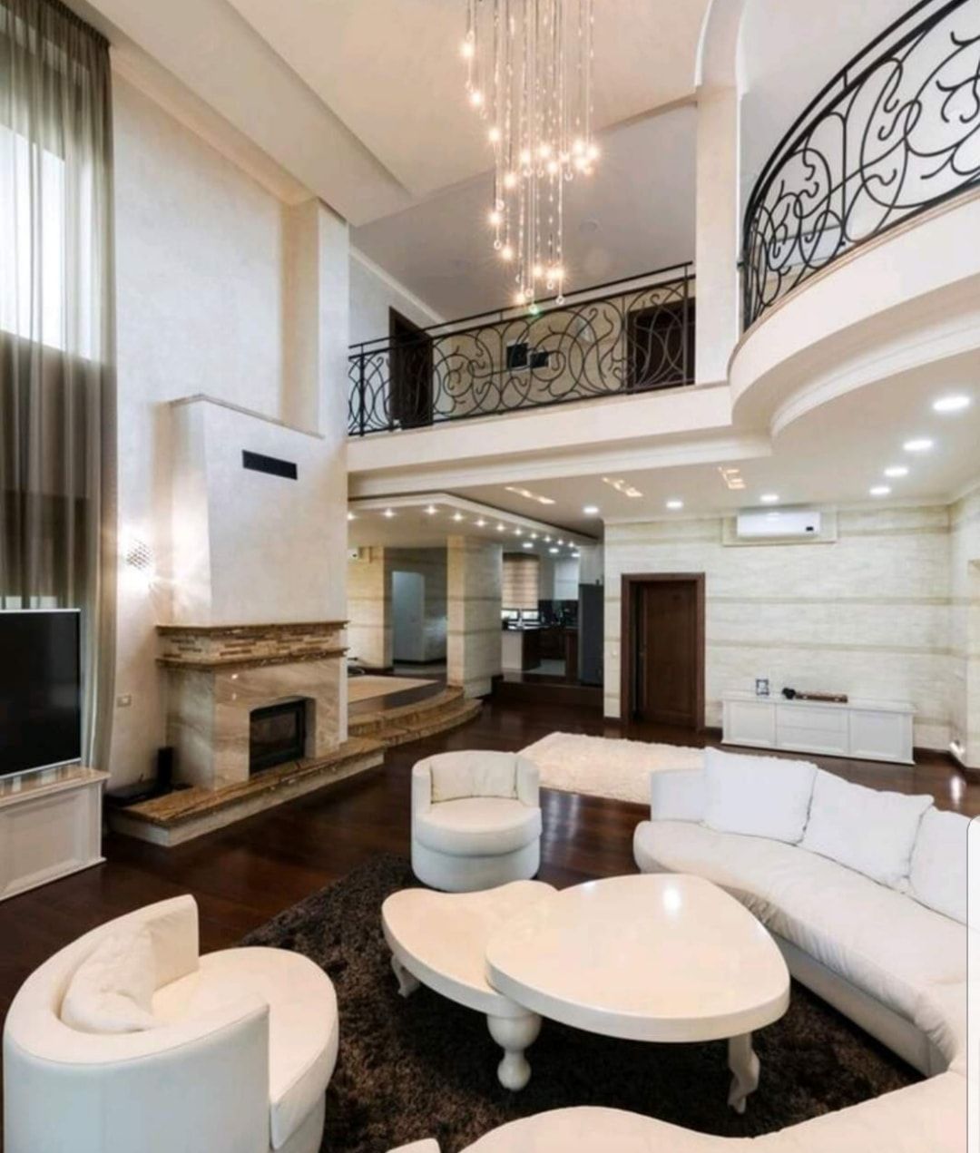 Spacious modern living room with white sectional, round tables, fireplace, and high ceiling with chandelier.