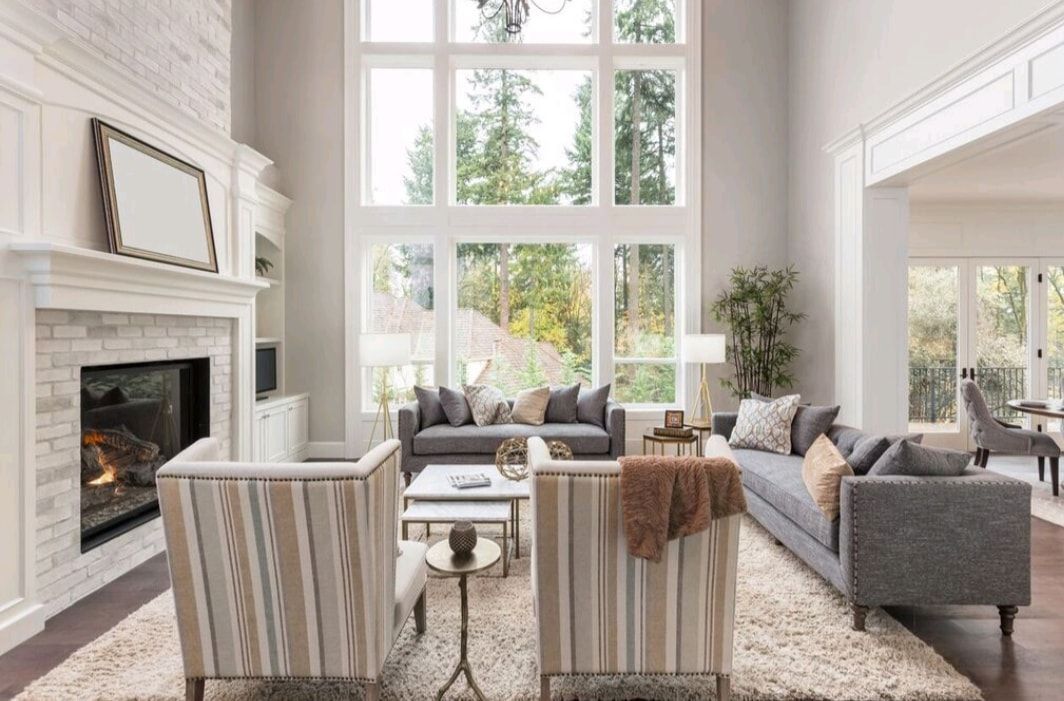 Bright living room with tall windows, white fireplace, gray sofas, and neutral decor