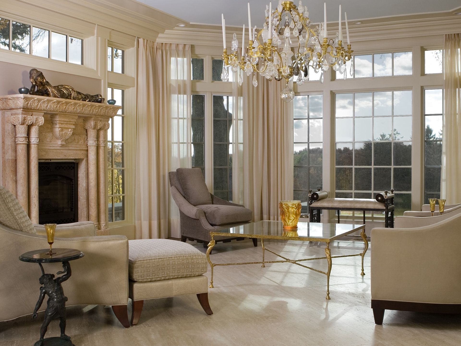 Elegant living room with tall windows, chandelier, fireplace, and cream-colored seating